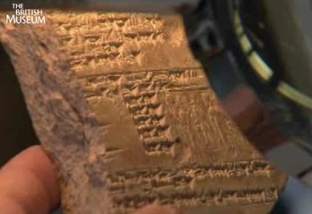 A screenshot showing a curator holding a tablet with ancient writing on it. 