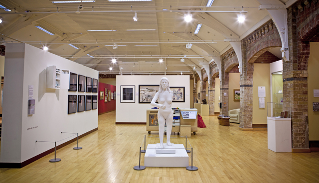 Interior of an art gallery with white walls and wooden floors with a white marble statue in the centre