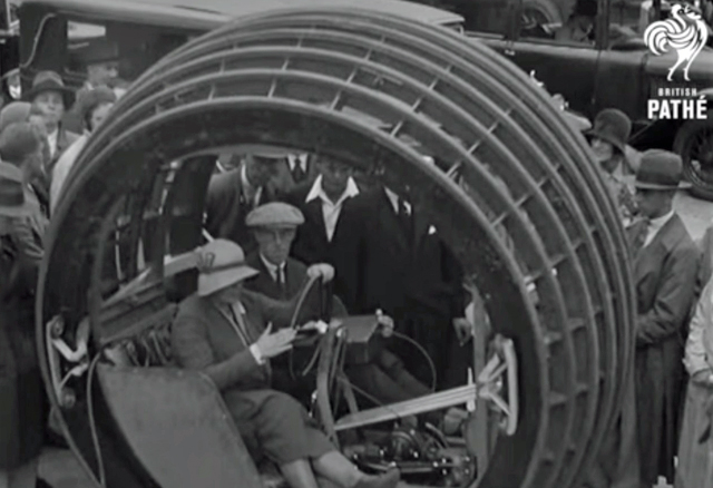 A black and white screen shot showing a woman in a strange vehicle