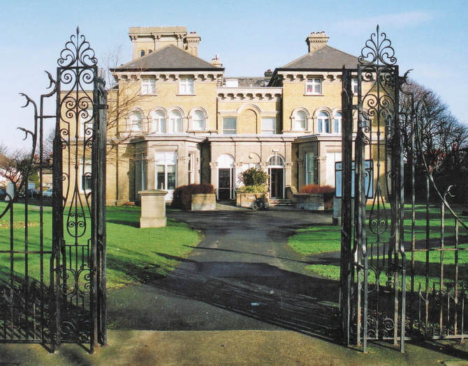 A large cream brick building seen from open wrought iron gates