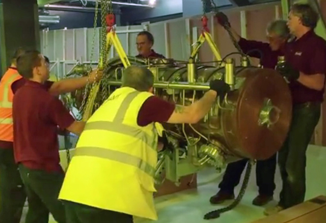A screenshot showing a group of people moving a large piece of equipment. 