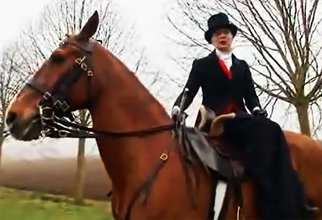 A screenshot showing a woman dressed in Victorian costume riding side saddle on a horse