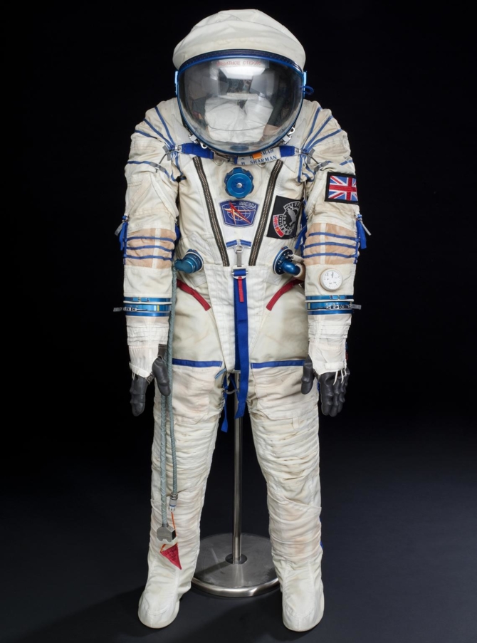 Blue and white spacesuit and helmet, with Union flag patch on the sleeve and 'Juno' space mission patch.