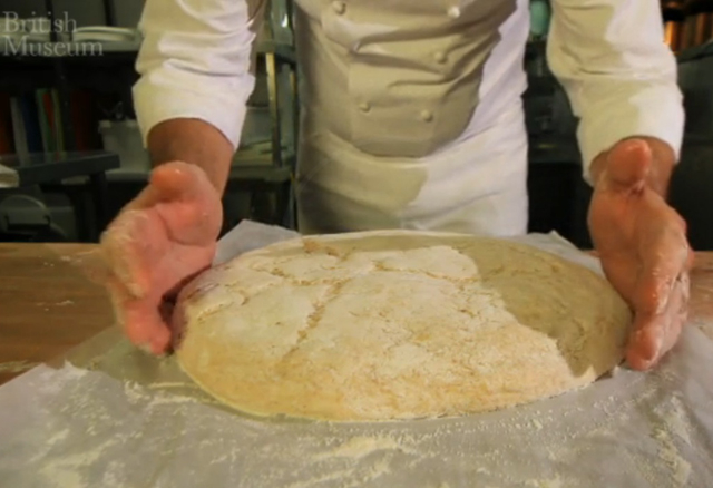 A screenshot showing a chef presenting a loaf of round bread. 